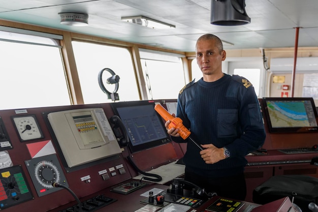 Offizier auf Wache mit SART auf der Navigationsbrücke Kaukasischer Mann in blauem Uniformpullover mit Such- und Rettungsradar-Transponder auf der Brücke eines Frachterschiffs