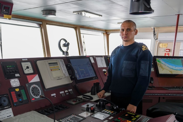 Oficial de guardia en el puente de navegación Hombre caucásico con suéter de uniforme azul en el puente del buque de carga
