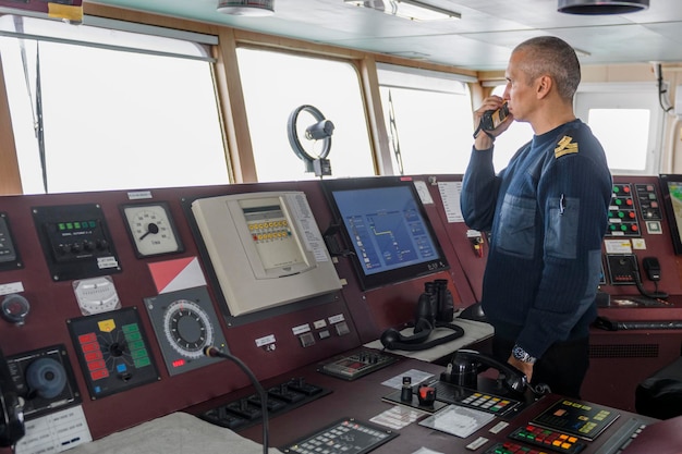 Foto oficial de guardia con radio en el puente de navegación hombre caucásico con suéter de uniforme azul en el puente del buque de carga