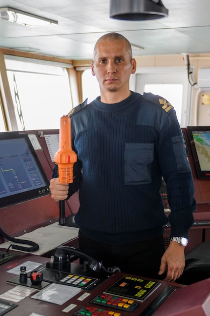 Oficial de guardia con SART en el puente de navegación Hombre caucásico con suéter de uniforme azul usando un transpondedor de radar de búsqueda y rescate en el puente del buque de carga
