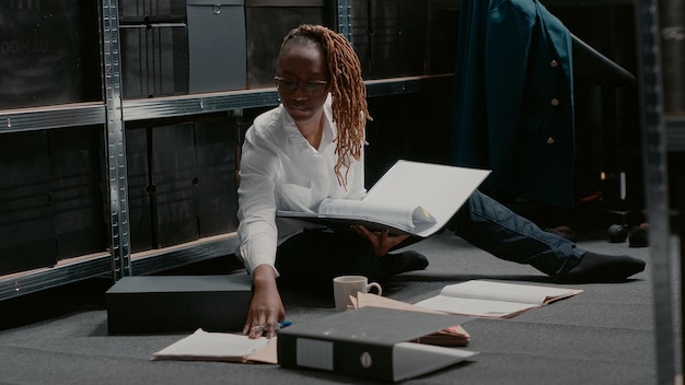 Oficial de la ley enfocado examinando archivos de casos en carpetas, leyendo importantes pistas criminales en el piso de archivo de la policía. Mujer inspectora investigando para encontrar sospechosos con fotos de vigilancia. Disparo de mano.