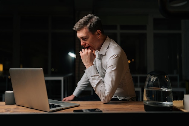 Oficial de personal masculino cansado bostezando mientras usa una computadora portátil sintiéndose somnoliento después de haber trabajado demasiado