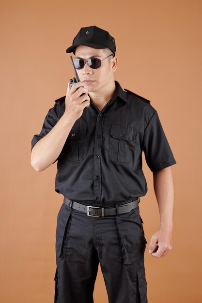 Oficial de policía con gorra de uniforme negro y gafas de sol hablando en walkietalkie