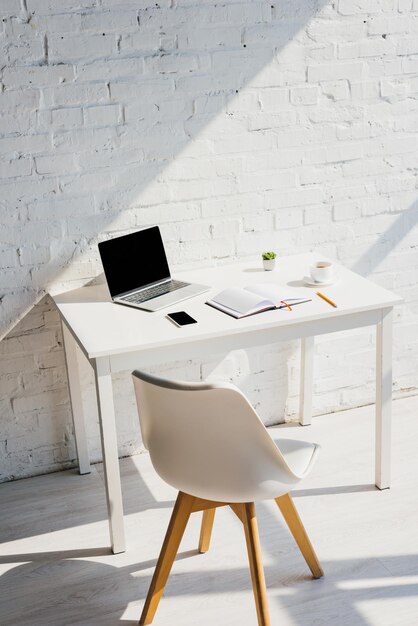 Foto oficina en casa con computadora portátil, teléfono inteligente, café y silla a la luz del sol