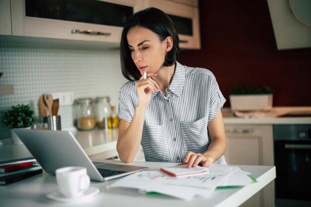 Oficina en casa Freelancer Linda mujer joven moderna en ropa informal usando una computadora portátil mientras trabaja en la habitación doméstica