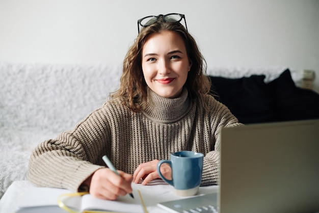 Oficina en casa de una joven tutora de inglés con café portátil y notas preparándose para la lección en línea