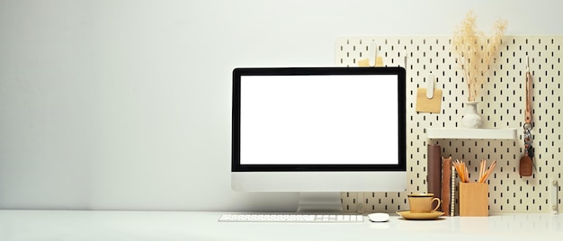 Oficina en casa con monitor de computadora en blanco, libros, taza de café y portalápices, mesa blanca, espacio para copiar para su diseño publicitario