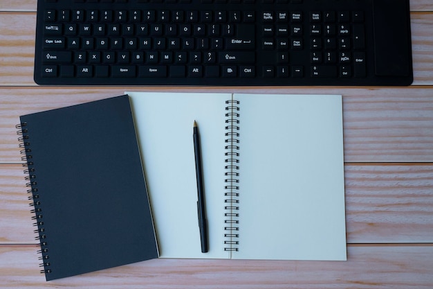 Oficina en casa con teclado, cuadernos y bolígrafo sobre mesa de madera. Espacio para texto. Plano, vista superior