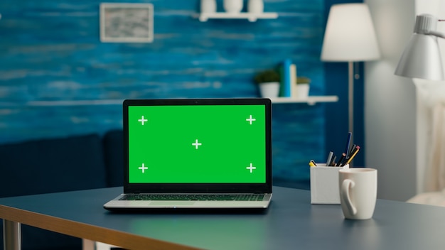 La oficina en casa vacía sin nadie en ella está lista para cursos de comunicación en línea usando una computadora aislada. Ordenador portátil con mock up chroma key de pantalla verde sentado en el escritorio en la luminosa sala de estar