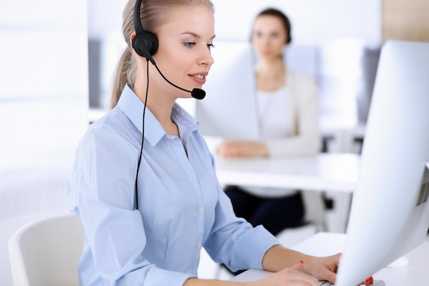 Oficina del centro de llamadas Hermosa mujer rubia usando computadora y auriculares para consultar a clientes en línea Grupo de operadores que trabajan como ocupación de servicio al cliente Concepto de personas de negocios