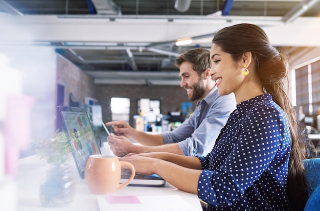 Oficina de coworking y mujer en el escritorio con una sonrisa de computadora portátil y hombre en una agencia creativa trabajando juntos en un proyecto Asociación de colaboración y empleados felices o socio comercial en el inicio del diseño