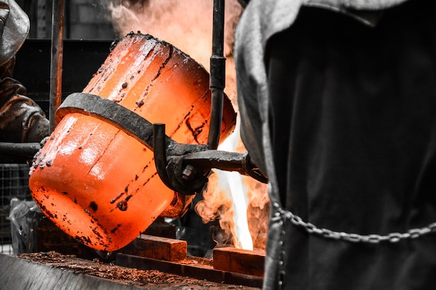 Oficina de fundição O metal fundido é derramado em um molde a partir de um cadinho manobrado por dois trabalhadores