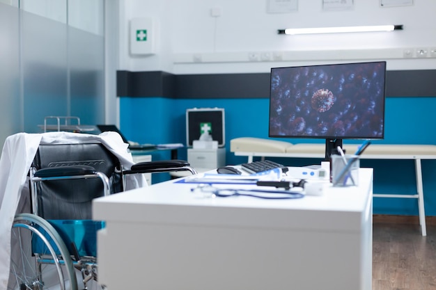 Oficina de examen vacía con computadora de pie en la mesa de escritorio con ilustración de cornavirus en la pantalla durante la pandemia global de covid19. Sala de hospital equipada con herramientas profesionales. imagen viral