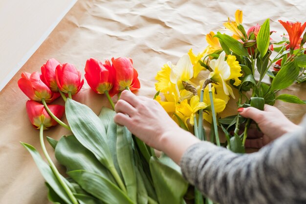 Oficina floral. mulher com as mãos fazendo um arranjo de flores de variedade de tulipas vermelhas, narciso amarelo e alstroemeria.