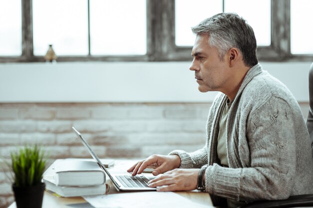 En la oficina. Hombre inteligente serio escribiendo en el teclado mientras está en el trabajo