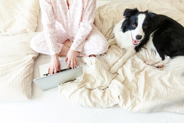 Oficina móvil en casa. mujer joven en pijama sentado en la cama con un perro mascota trabajando usando la computadora portátil pc en casa. chica de estilo de vida estudiando en el interior. concepto de cuarentena empresarial independiente.