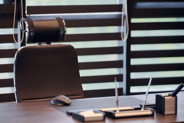 Oficina de negocios. Lugar de trabajo para jefe, jefe u otros empleados. Mesa y silla cómoda. Luz a través de las persianas medio abiertas