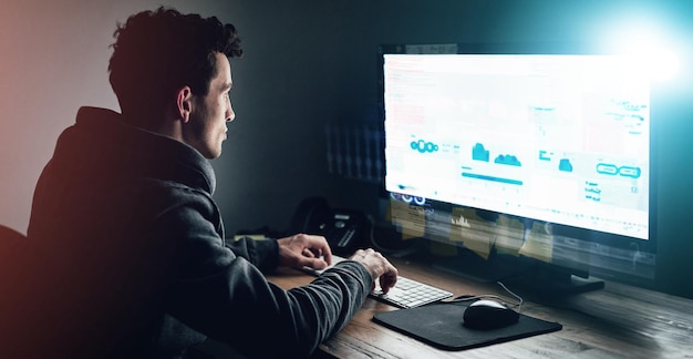 Oficina oscura y hombre en la computadora para el análisis de datos programación en línea y ciberseguridad en la pantalla Software cripto y desarrollador web con tabla de instrumentos gráfico de acciones o piratería cibernética en el escritorio por la noche