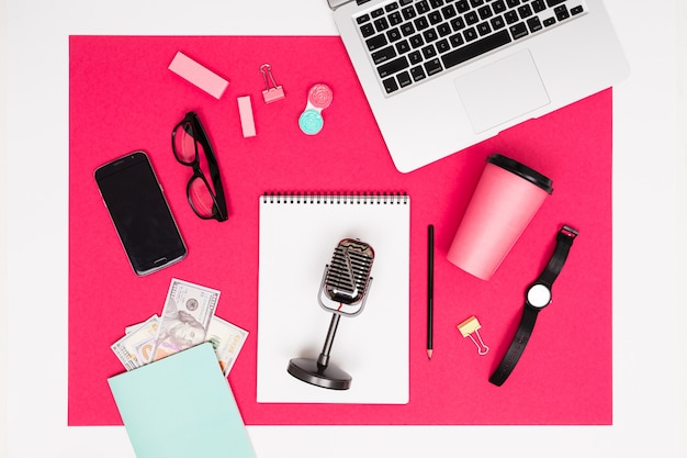 Oficina de trabajo. papelería, micrófono, teléfono y computadora portátil y dinero se encuentran en una mesa rosa con un marco