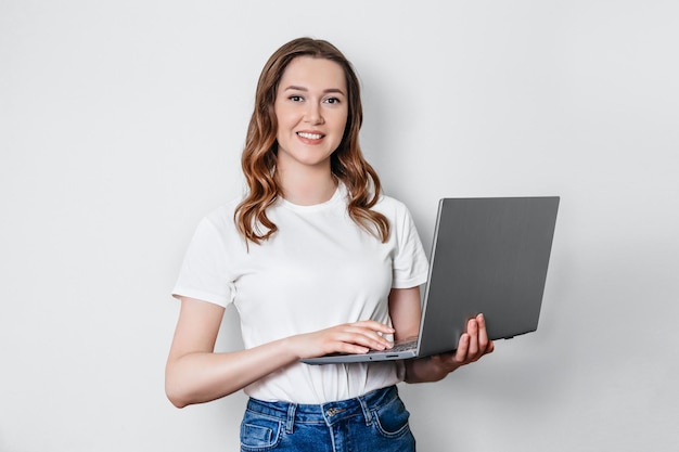 Oficinista caucásica sonriente de la empresaria en camiseta blanca que usa la computadora portátil