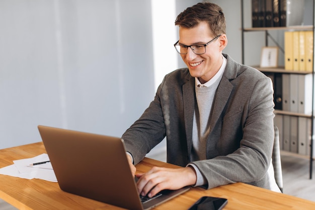 Oficinista de hombre sonriente moderno que trabaja en la computadora portátil