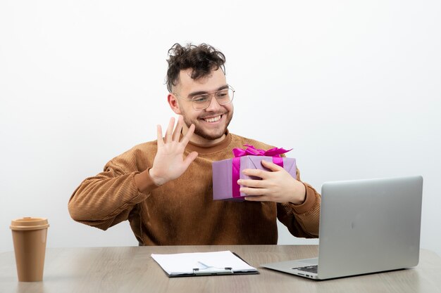 Oficinista masculino sentado en el escritorio con su regalo de vacaciones.