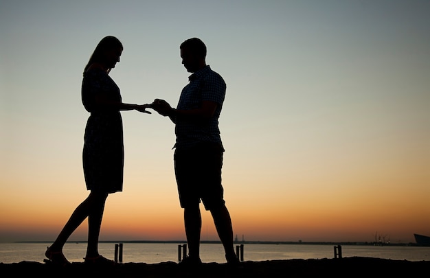 Ofrezca su mano y su corazón en la playa en el contexto de una hermosa puesta de sol, compromiso Un hombre le da un anillo y le pide a una niña que se case, ella es feliz