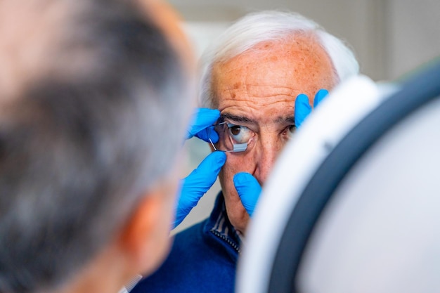 Foto oftalmólogo colocando un abridor de ojos a un hombre mayor