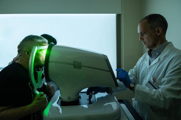 Foto oftalmólogo tratando el glaucoma en un anciano usando una máquina láser