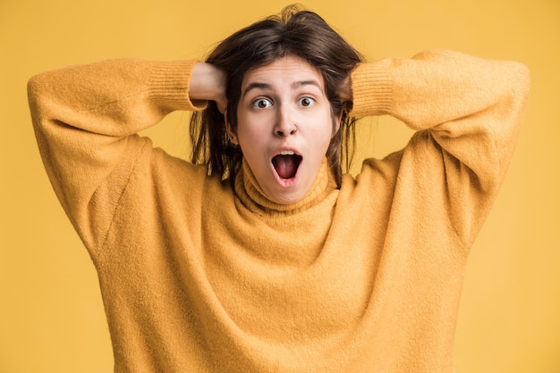 Oh meu Deus, uau. Retrato de mulher espantada, olhando para a câmera com expressão chocada e mantendo as mãos no rosto, gritando de surpresa. Foto de estúdio interna isolada em fundo amarelo