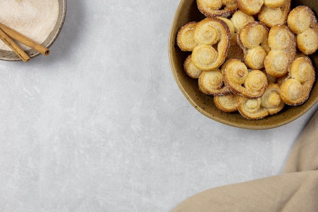 Ojal de hojaldre, galletas Palmier en un recipiente con canela y azúcar en el fondo de hormigón claro con espacio de copia.