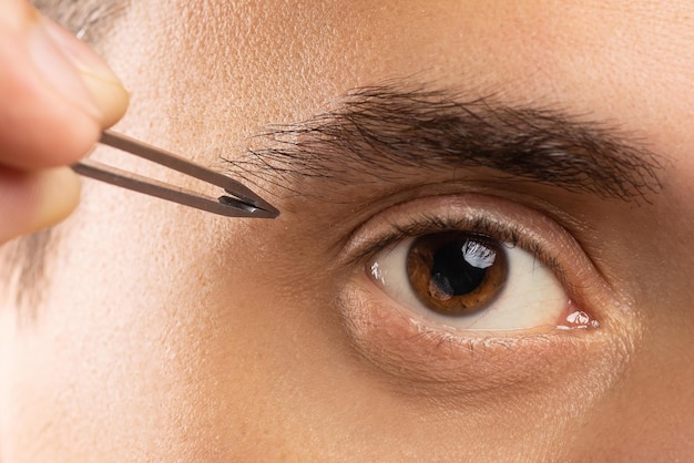 Foto ojo masculino y pinzas para corregir la forma de las cejas