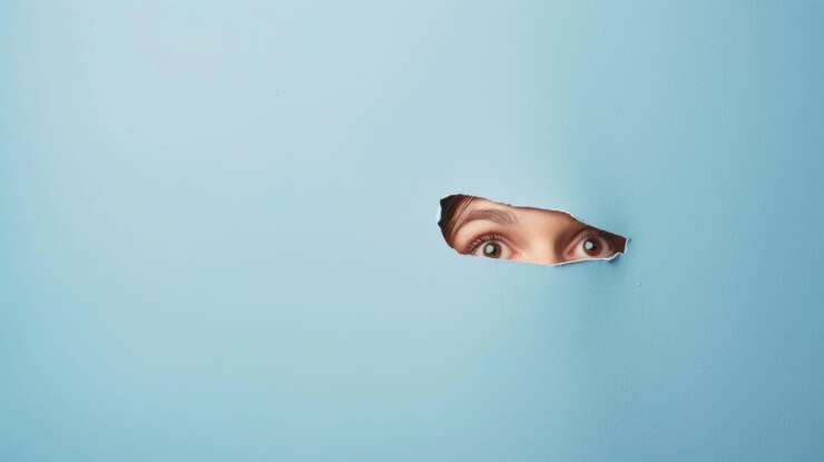El ojo de una mujer mira por un agujero en la pared azul