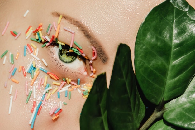 Foto un ojo de mujer verde abierto con un dulce rocío multicolor en el párpado y una planta con grandes hojas verdes