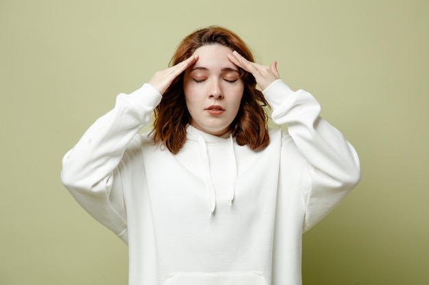 Con los ojos cerrados, poniendo las manos en la cabeza, una mujer joven con un suéter blanco aislado en un fondo verde