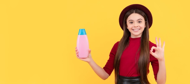 Ok, niña feliz con sombrero, sostenga champú que presenta un producto cosmético para adolescentes