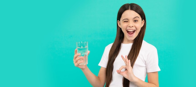 Ok, niño, sostenga un vaso de agua, el niño se siente sediento, una adolescente va a beber una bebida mineral, una pancarta de una niña con un vaso de agua, un retrato de estudio con espacio para copiar.