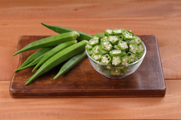 Okra o Ladys finger o Bhindi vegetales verdes frescos dispuestos en una tabla de madera con un recipiente de vidrio lleno de anillos en rodajas de okra con enfoque selectivo de fondo de madera