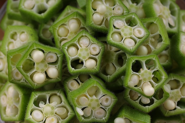 Okra oder Ladys Finger oder Bhindi frisches grünes Gemüse, angeordnet auf einem Holzbrett mit einer Glasschüssel voller Okra geschnittener Ringe mit selektivem Fokus aus Holzhintergrund