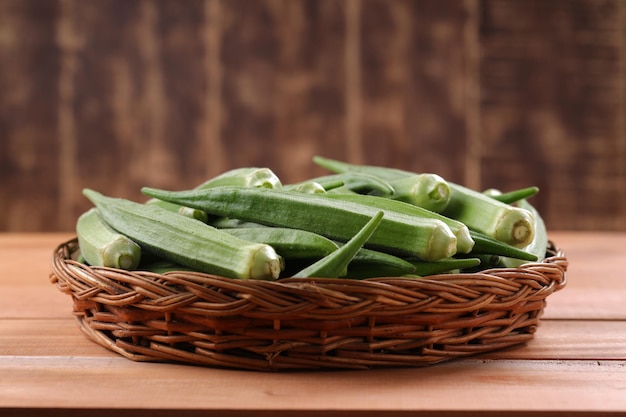 Okra oder Ladys Finger oder Bhindi frisches grünes Gemüse, angeordnet in einem Korb mit hölzernem strukturiertem Hintergrund, isoliert und selektiver Fokus