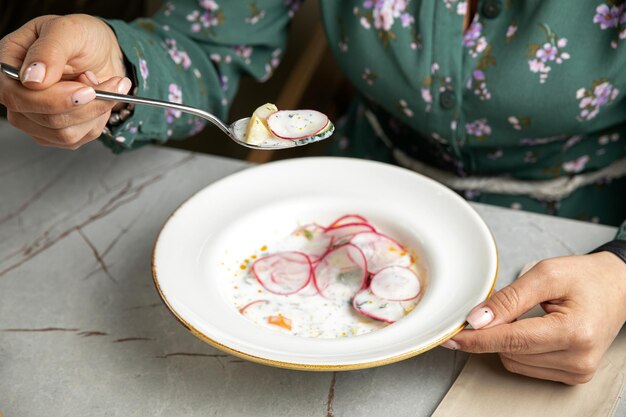 okroshka com rabanetes pepinos ervas e iogurte em uma mesa cinza