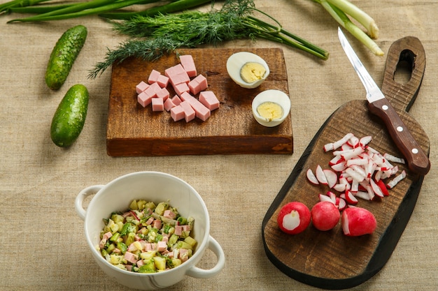 Foto okroshka em uma terrina na mesa em uma toalha de mesa ao lado de vegetais nas placas. foto horizontal