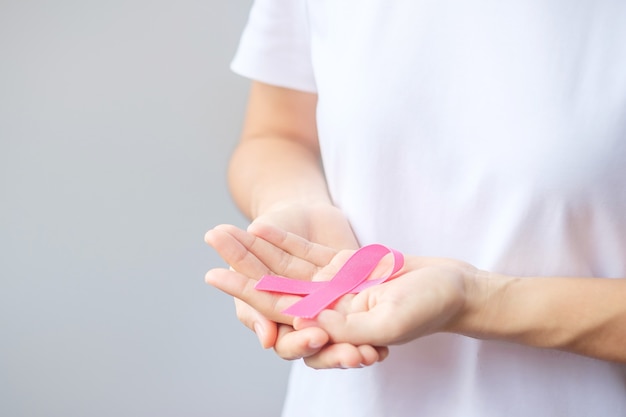 Oktober Brustkrebs-Bewusstseinsmonat, ältere Frau im weißen T-Shirt mit der Hand, die Pink Ribbon hält, um Menschen zu unterstützen, die leben und krank sind. Konzept des Internationalen Frauen-, Mutter- und Weltkrebstages