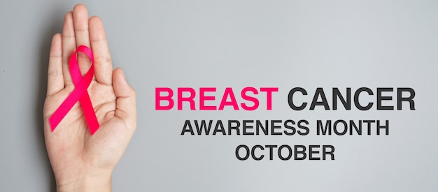 Oktober Brustkrebs-Bewusstseinsmonat, erwachsene Frauenhand, die rosa Band auf grauem Hintergrund für die Unterstützung lebender Menschen und Krankheit hält. Internationales Konzept für Frauen, Mutter und Weltkrebstag