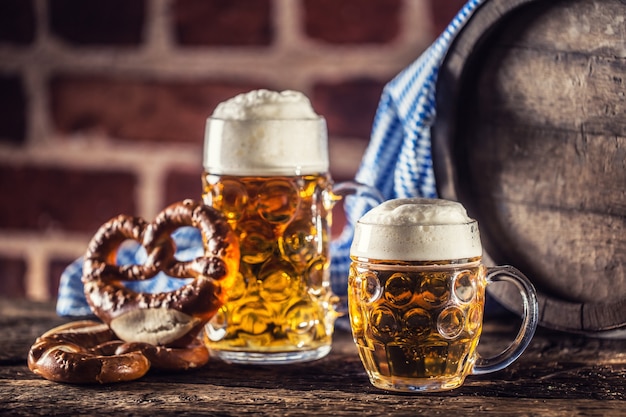 Foto oktoberfest cerveja grande e pequena com barril de madeira pretzel e toalha de mesa azul.