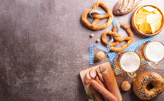 Oktoberfest-Dekorationssymbole aus Brezellaib-Bierwurst-Kartoffelchips und bayerischem weißem und blauem Stoff auf dunklem Steinhintergrund