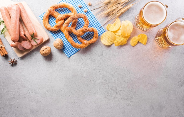 Oktoberfest-Dekorationssymbole aus Brezellaib-Bierwurst-Kartoffelchips und bayerischem weißem und blauem Stoff auf Steinhintergrund