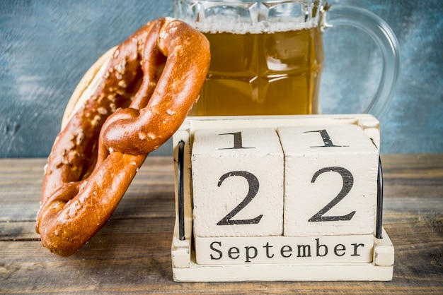 Foto oktoberfest-feier-konzept mit bierglaskrug, brezel und alten retro-stil holzkalender, blauen und hölzernen hintergrund,