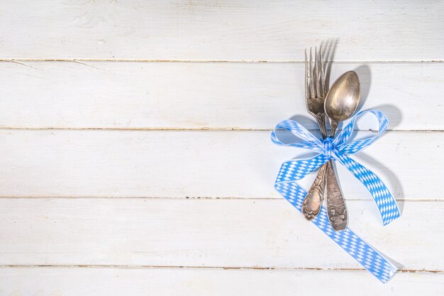 Oktoberfest-Konzept. Oktoberfest-Gedeckhintergrund, Tellergabelmesserlöffel mit traditioneller Serviette, Bierkrug. serviert bei Veranstaltung, Bar-Menü Flatlay, weißer Holztisch Kopie Raum Draufsicht top