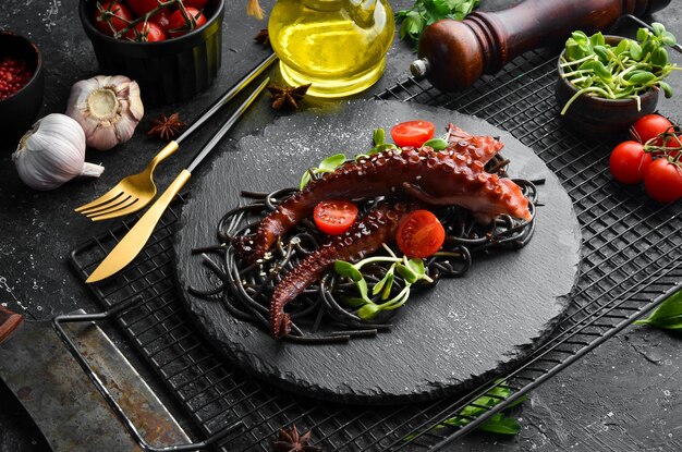 Oktopus-Tentakel gebacken in Knoblauchsauce und schwarze Nudeln mit Tintenfischtinte Luxus-Restaurant-Essen Meeresfrüchte Rustikaler Stil Flat Lay